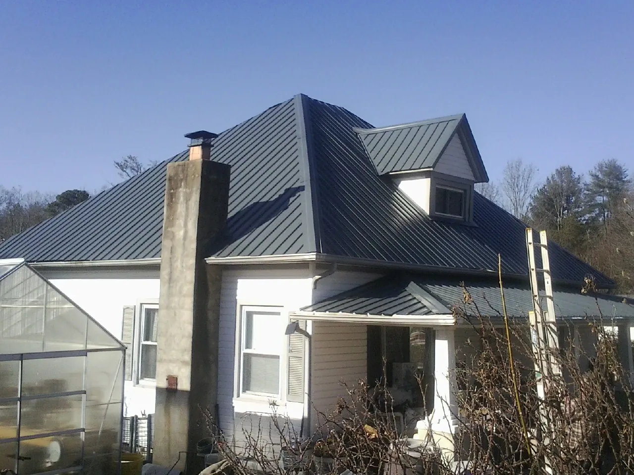 Dark blue standing seam metal roof on a white farmhouse with dormer — Slate & Tile Roof Repair by Roofing Brothers in Pryor