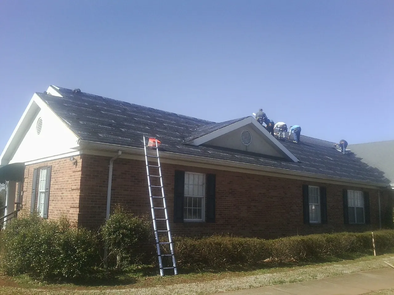 Crew tearing shingles off a brick ranch roof with a ladder set — Emergency Roof Repair work by our crew in Pryor