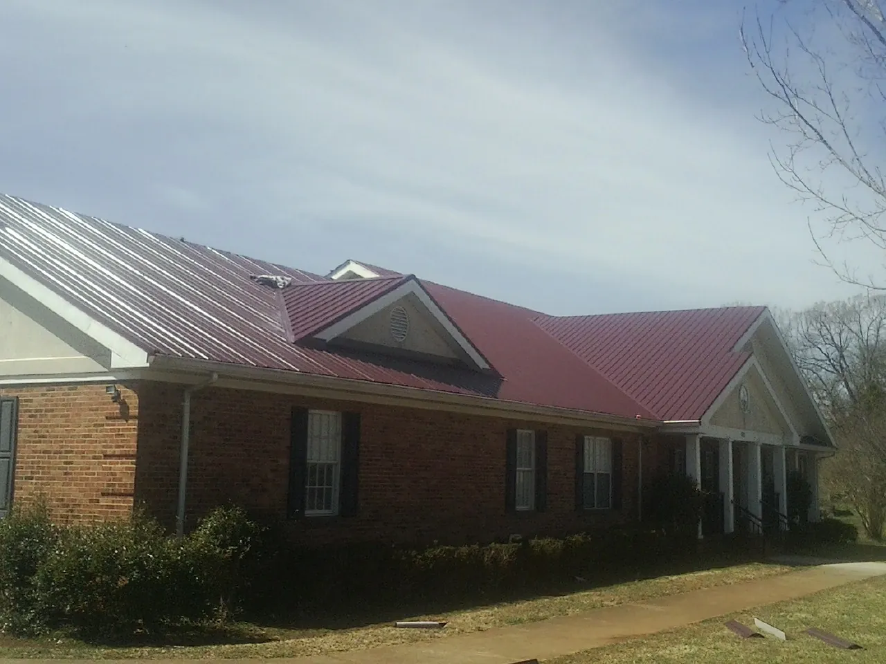 Red metal roof with gabled entries on a long brick building, from a Hail Damage Roof Repair job in Pryor