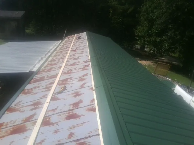 Old rusted panels beside newly installed green metal roofing — Wind Damage Roof Repair by Roofing Brothers in Pryor