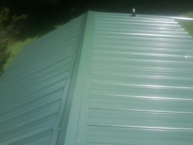 New green metal panels meeting at the ridge of a roof — Flat Roof Repair work by our crew in Pryor
