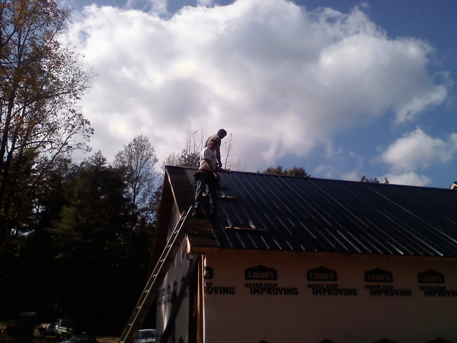 Roofer fastening dark metal panels high against a cloudy sky, from a Roof Inspection job in Pryor