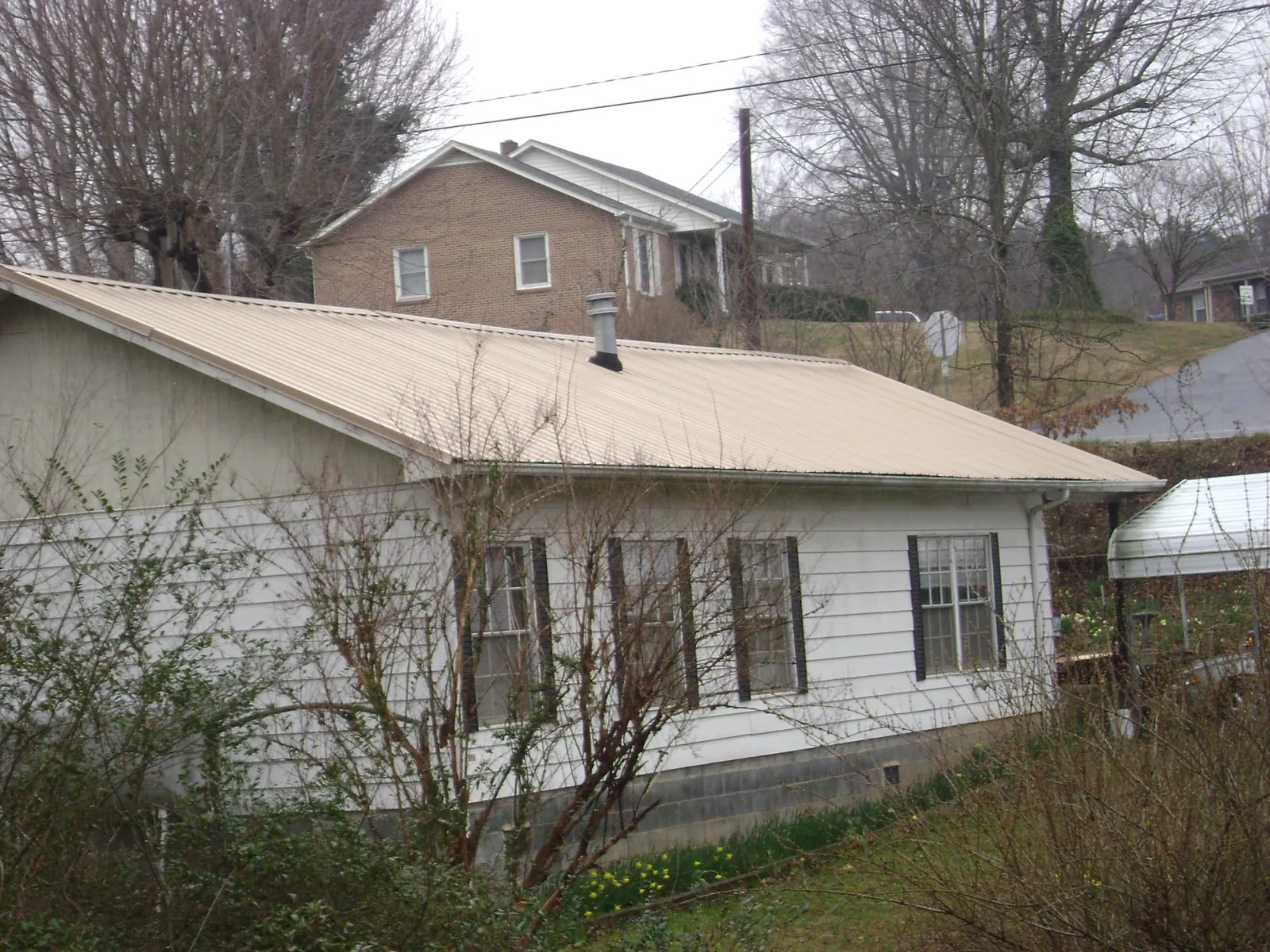 Tan metal roof on a white sided house set into a hillside — Commercial Roofing by Roofing Brothers in Pryor