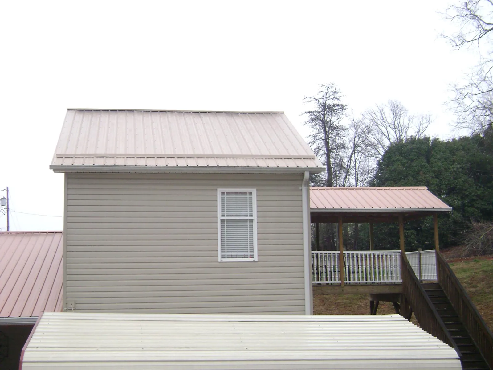 Tan metal roofs on a two story addition and attached porch, from a Roof Replacement job in Pryor